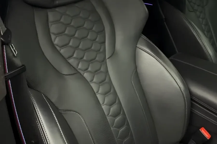 Luxurious black leather car seat with hexagon stitching and M logo after professional interior detailing.